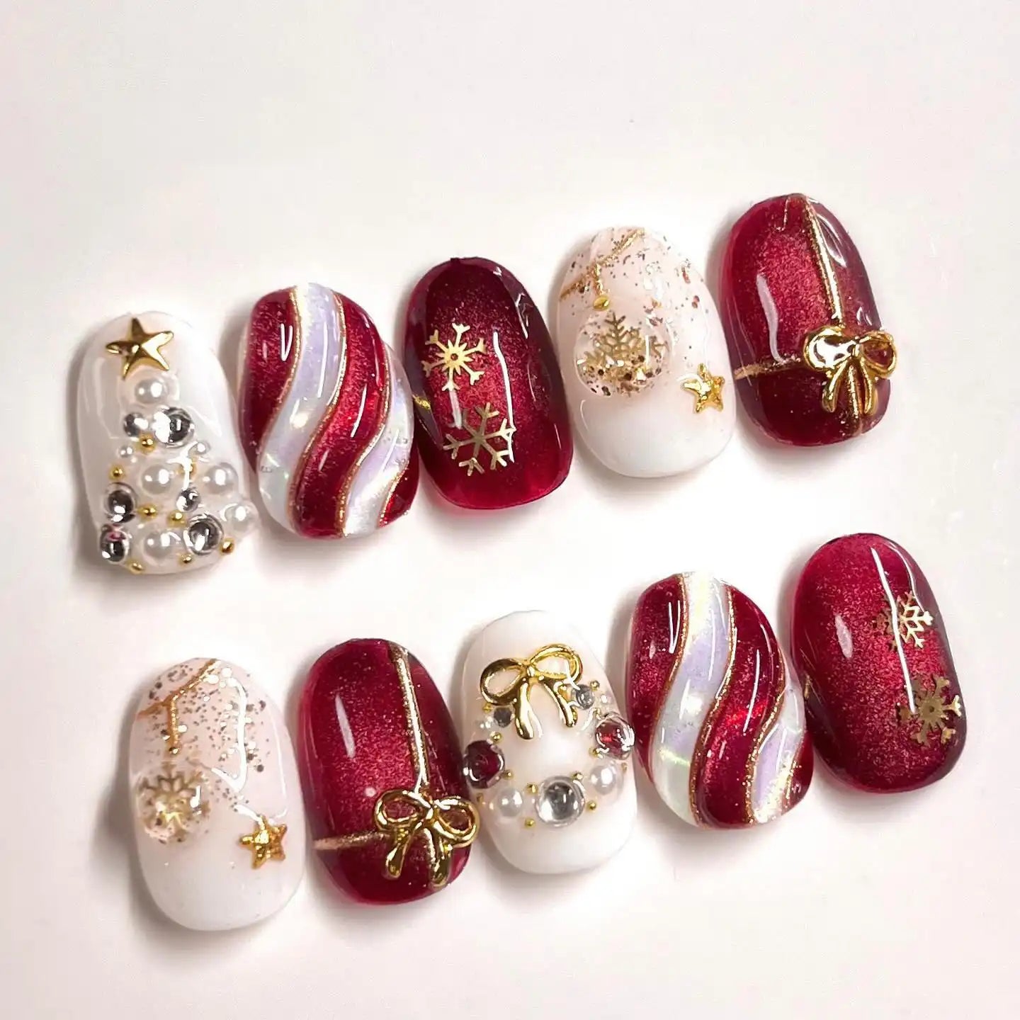 Handmade Christmas press-on nails with red glitter, gold bows, snowflakes, and pearl accents.