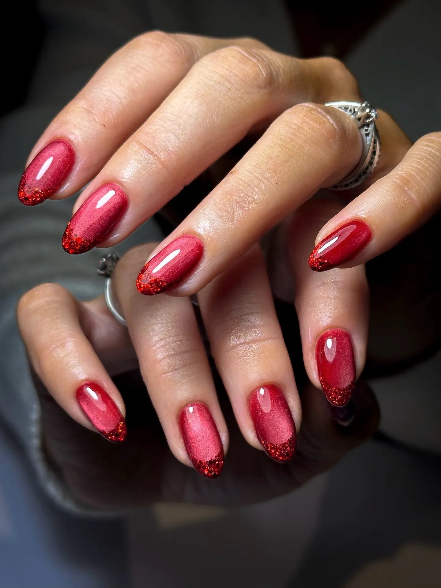 Hand with handmade ruby red shimmer gradient French tip press-on nails with glitter accents