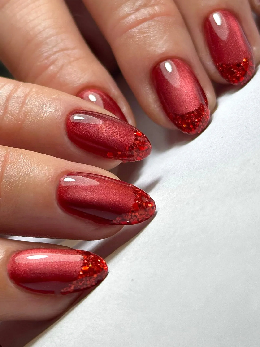 Hand with handmade ruby red shimmer gradient French tip press-on nails with glitter accents
