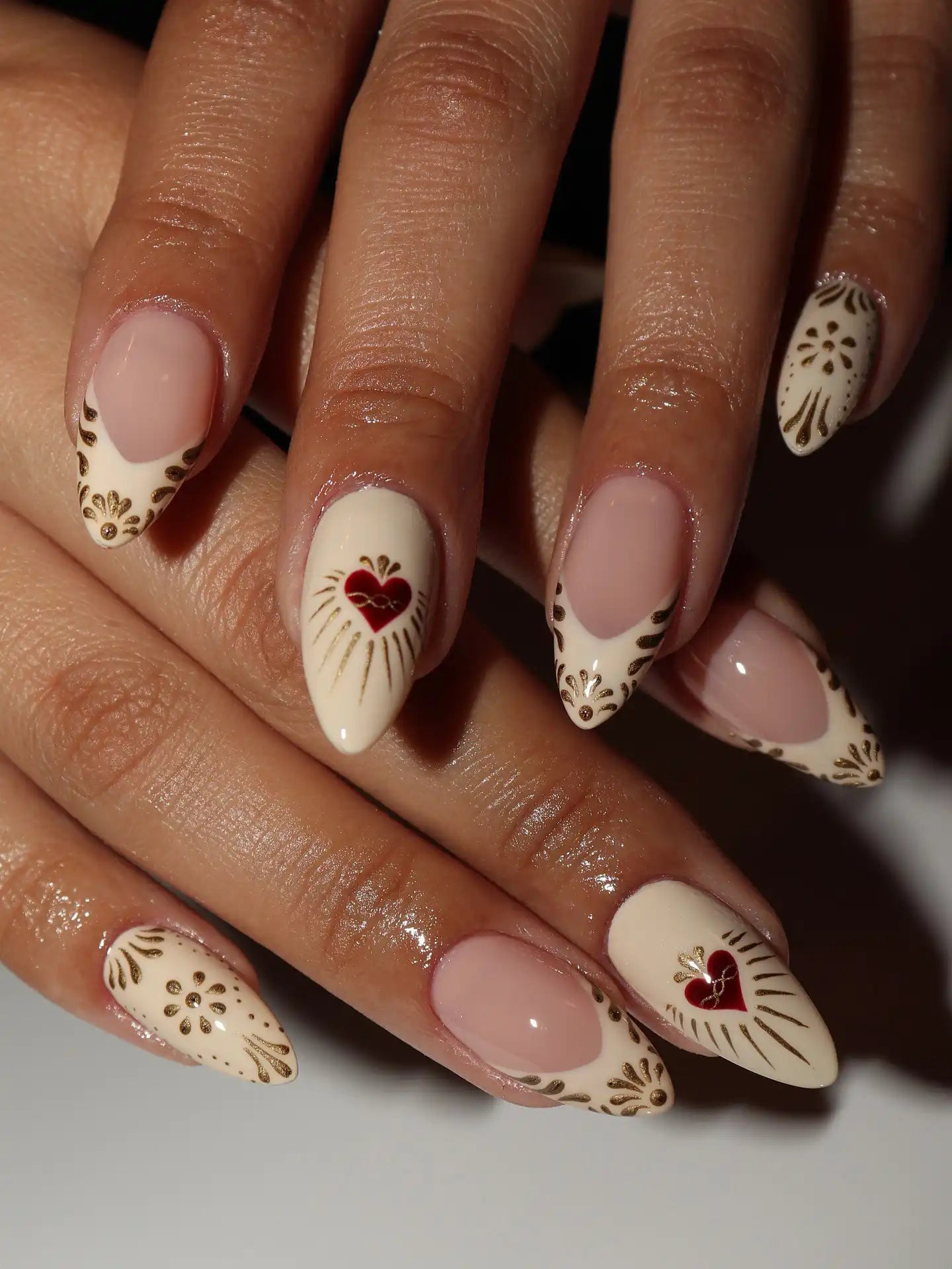 Hand with handmade press-on nails featuring gold ornate designs and red sacred heart art.