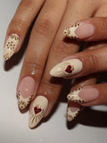 Handmade press-on nails with gold ornate patterns and red sacred heart accents on nude base