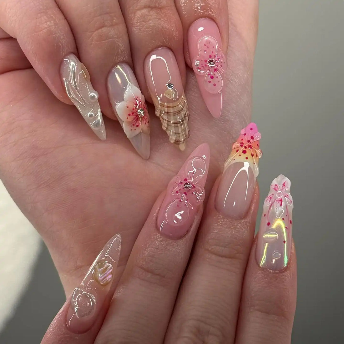 Hand with long, handmade press-on nails featuring 3D seashell and blossom flower designs.
