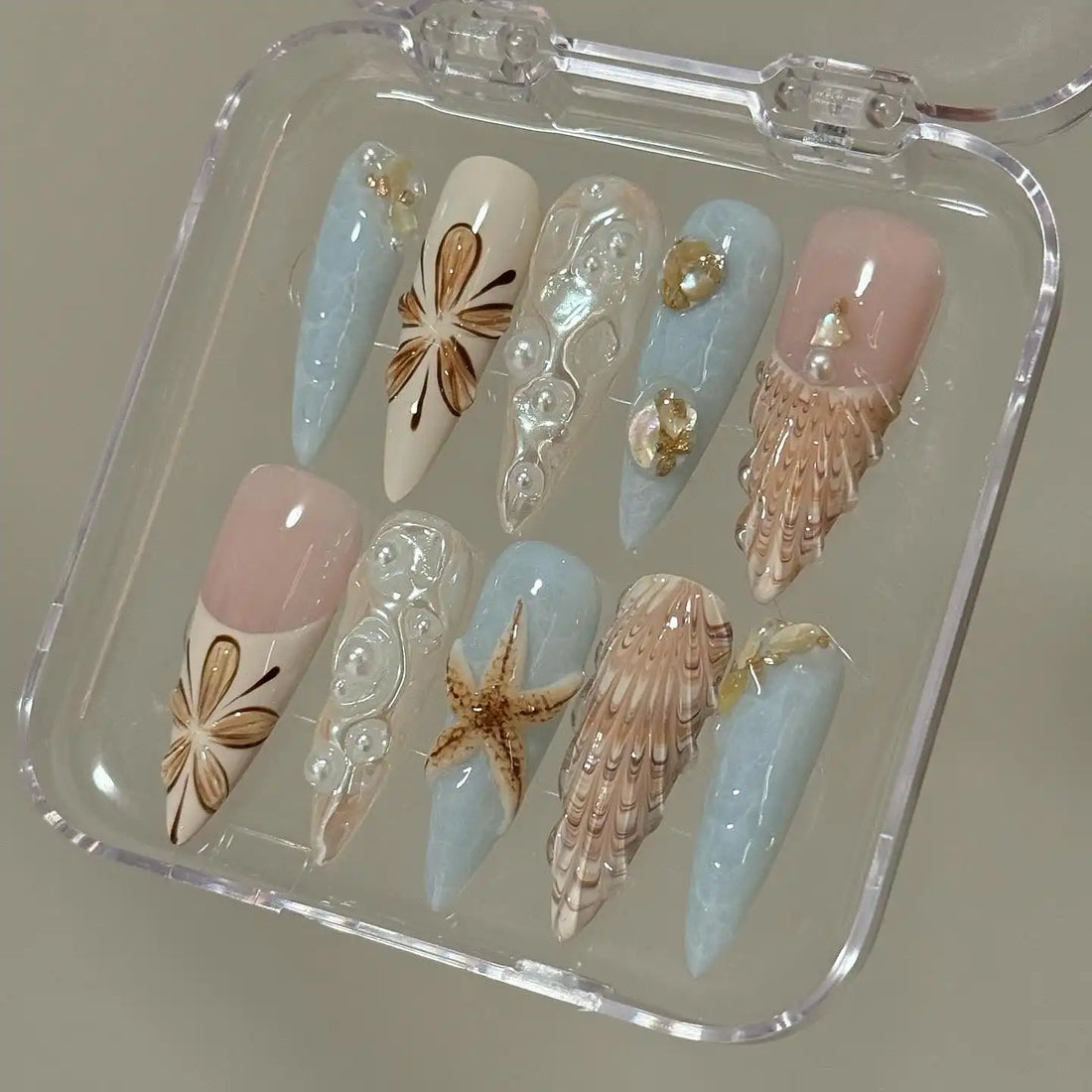 Handmade seashell and starfish press-on nails with ocean-themed 3D designs in blue and nude tones.