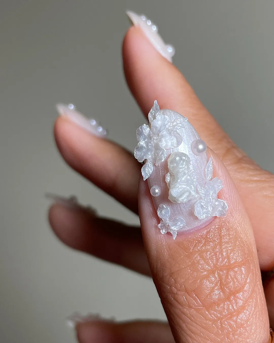 Hand with iridescent pearl 3D floral press-on nails featuring shimmering accents.