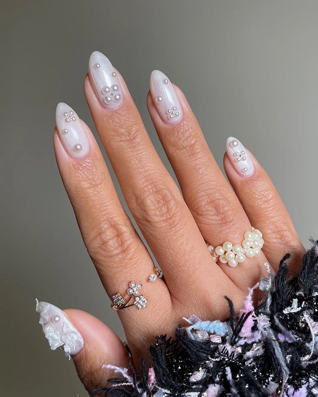 Hand with iridescent pearl 3D floral press-on nails, elegant rings, and a textured sleeve
