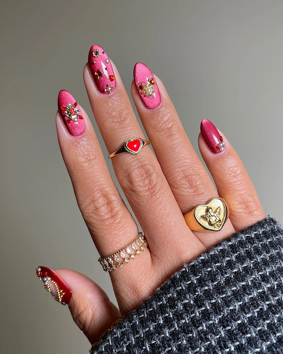 Hand with shimmering red and burgundy press-on nails, gold star and gemstone accents