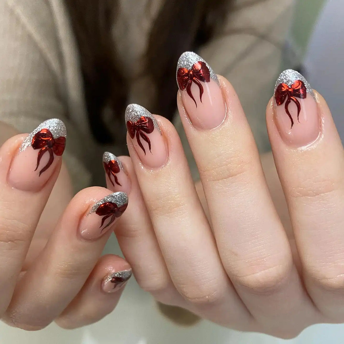 Handmade nude press-on nails with silver glitter tips and red Christmas bow designs