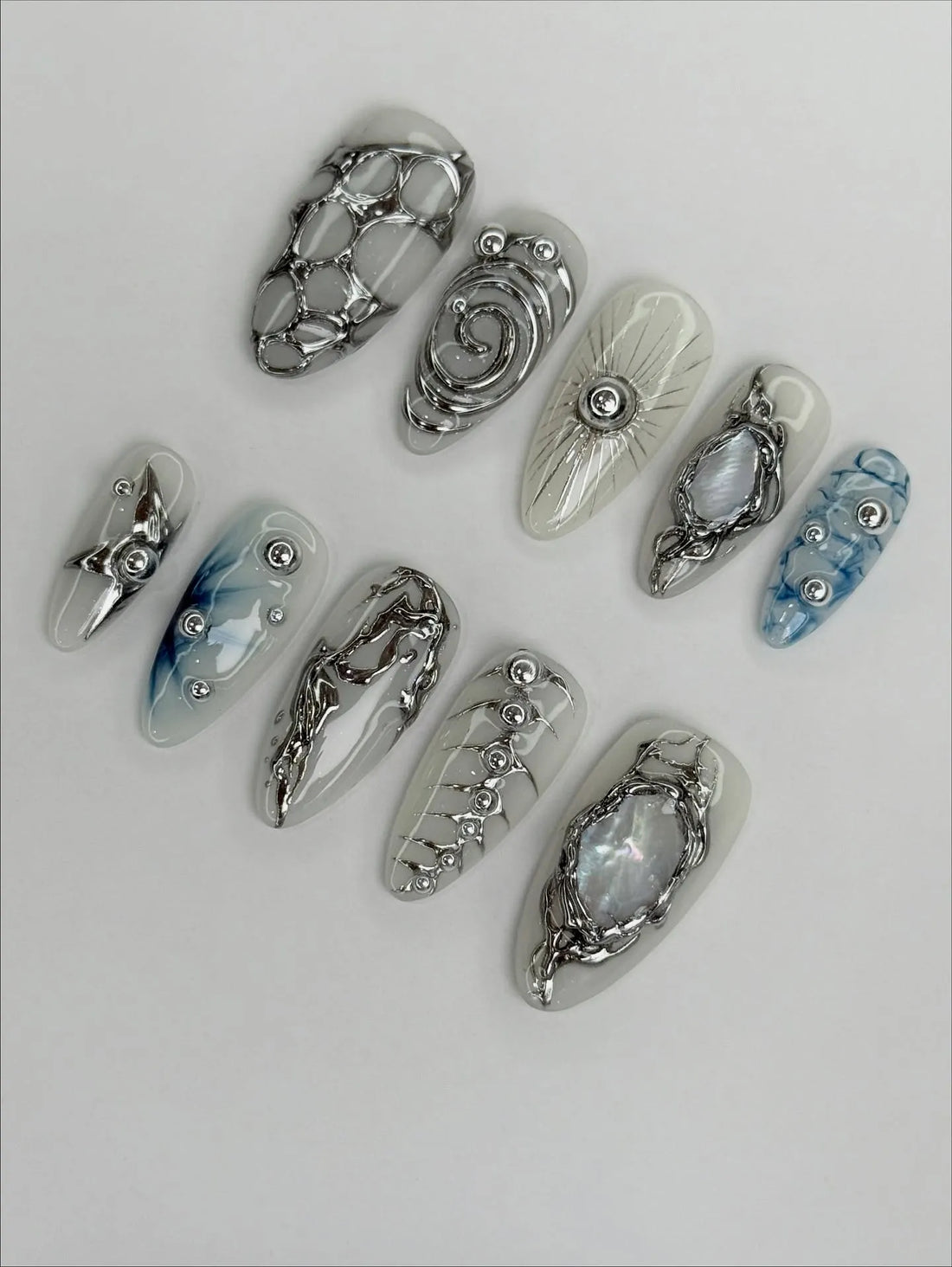 Handmade silver metallic chrome press-on nails with abstract and marble designs on white base.