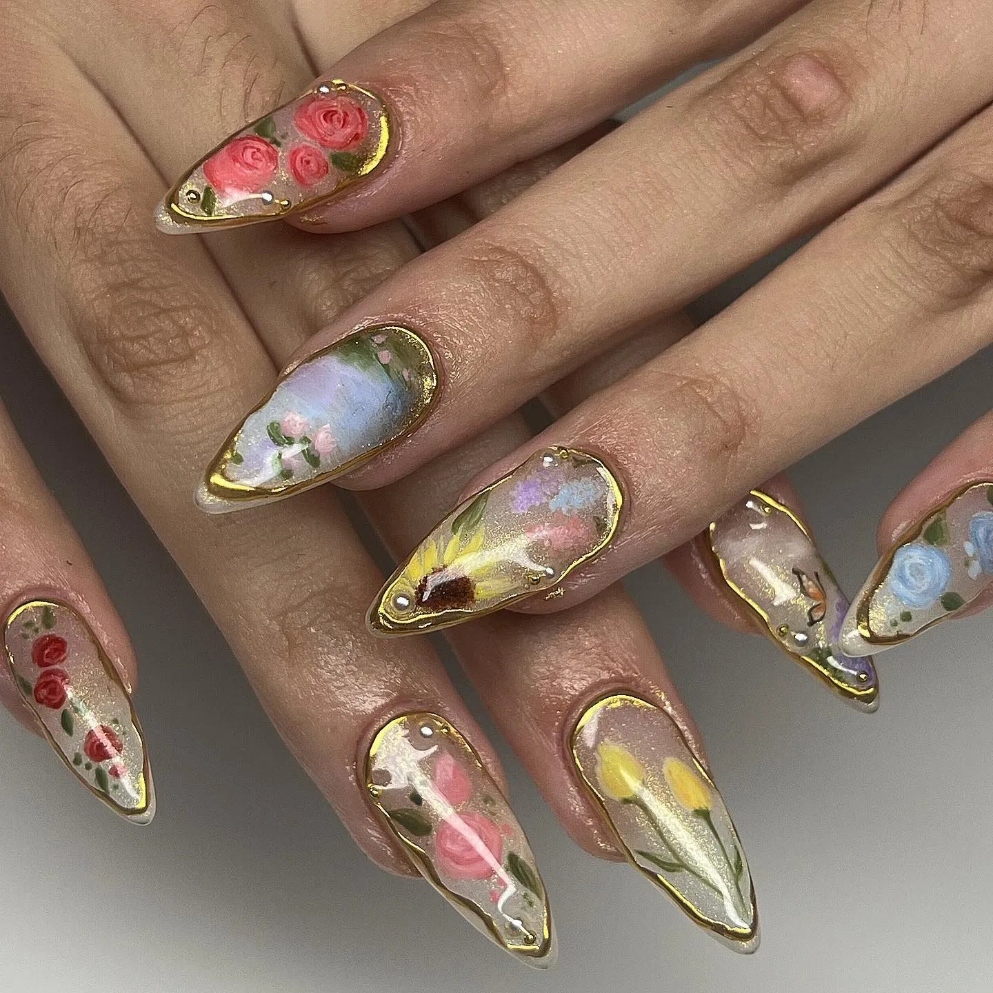 Handmade press-on nails with gold leaf edging and spring floral designs in pastel colors.