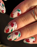 Hand with handmade press-on nails featuring red floral stained glass design on white base.