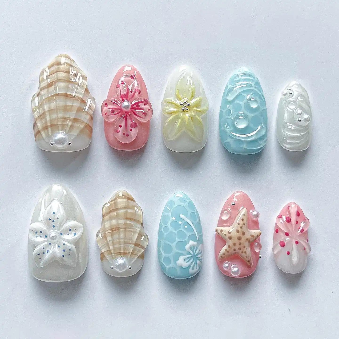 Handmade pastel beach press-on nails with starfish, seashell, and floral designs on white background.