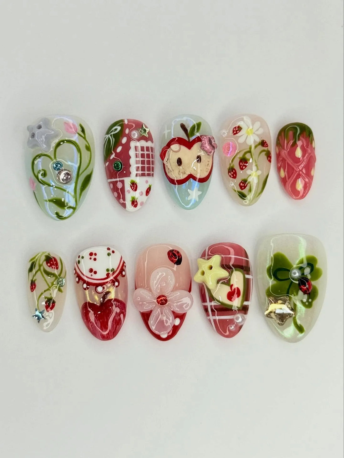 Handmade press-on nails with strawberry, apple, gingham, and floral designs, colorful gems