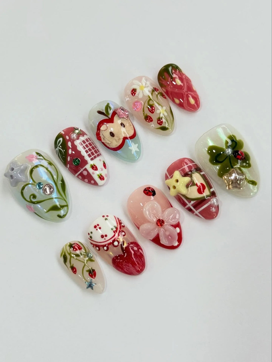 Handmade press-on nails with strawberry, apple, gingham, and floral designs, colorful gems