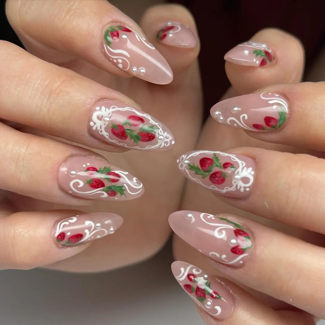 Handmade press-on nails with pink base, strawberry art, white lace accents, and pearl details