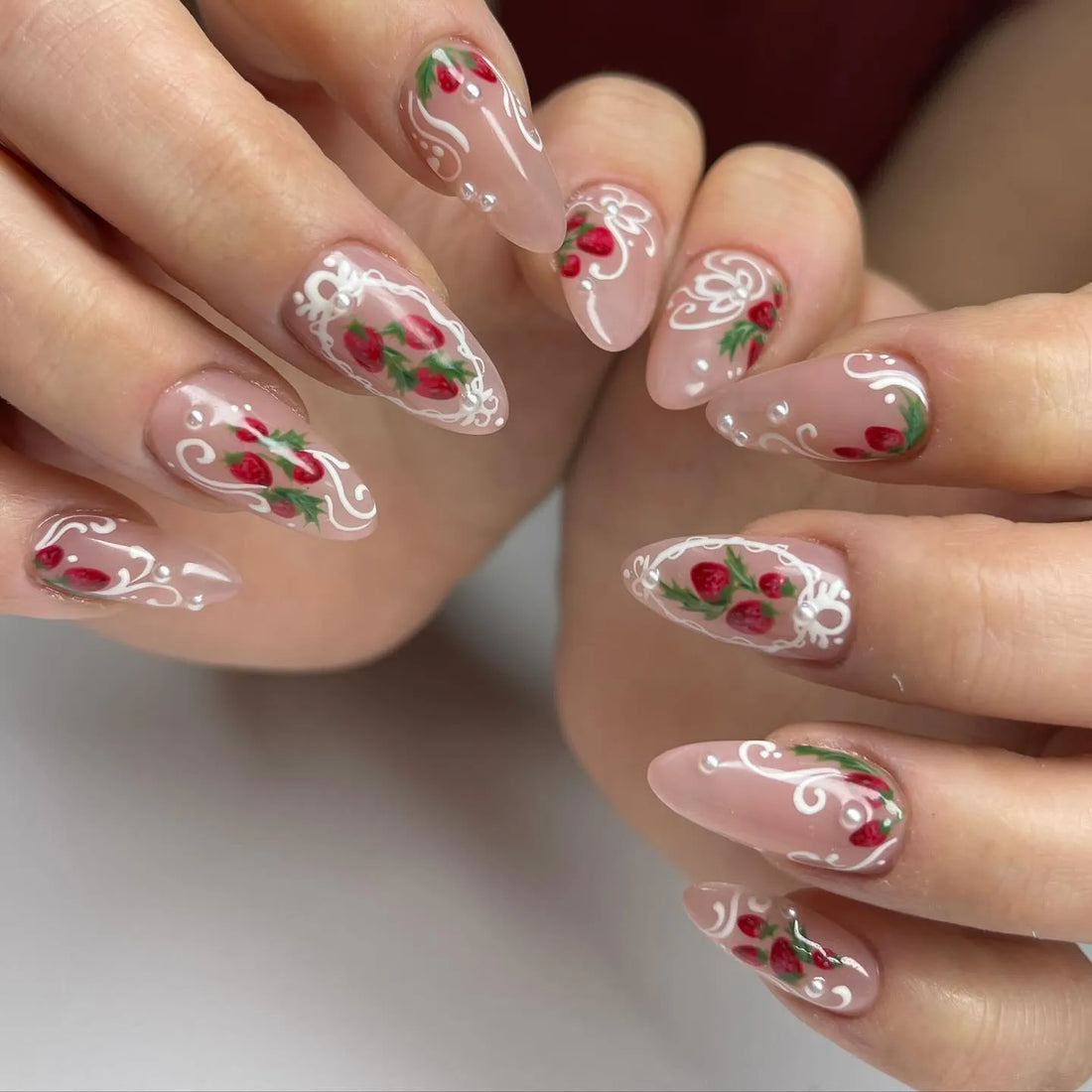 Handmade press-on nails with pink base, strawberry art, white lace accents, and pearl details