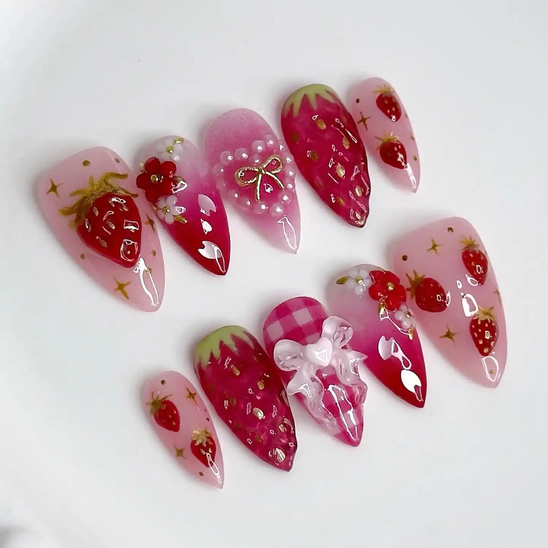 Handmade pink press-on nails with strawberry, floral, pearl, and bow designs