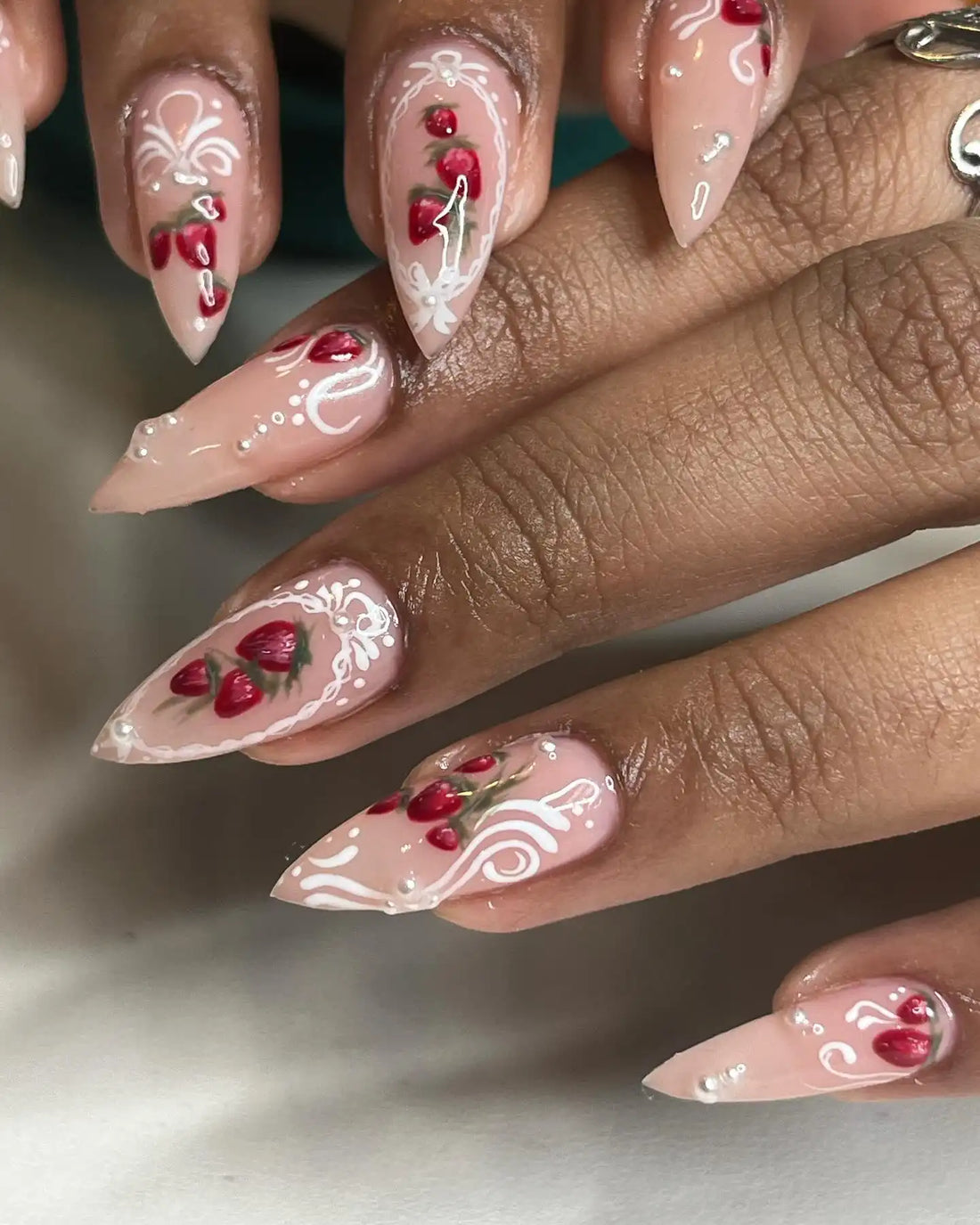 Handmade press-on nails with strawberry designs and white swirl accents on almond-shaped tips