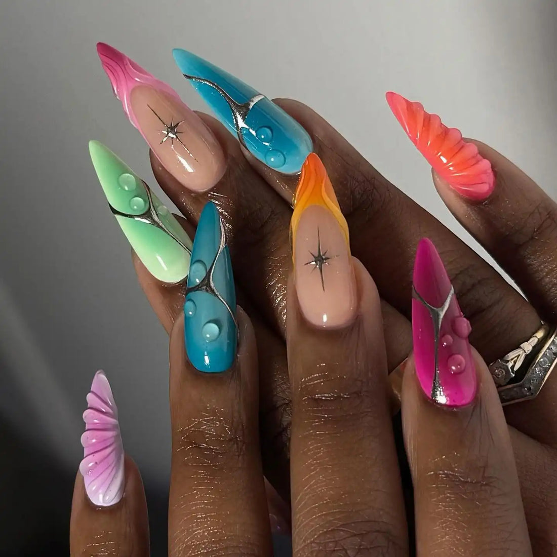 Hand with long press-on nails, featuring colorful gradient, shell, and summer-inspired designs.