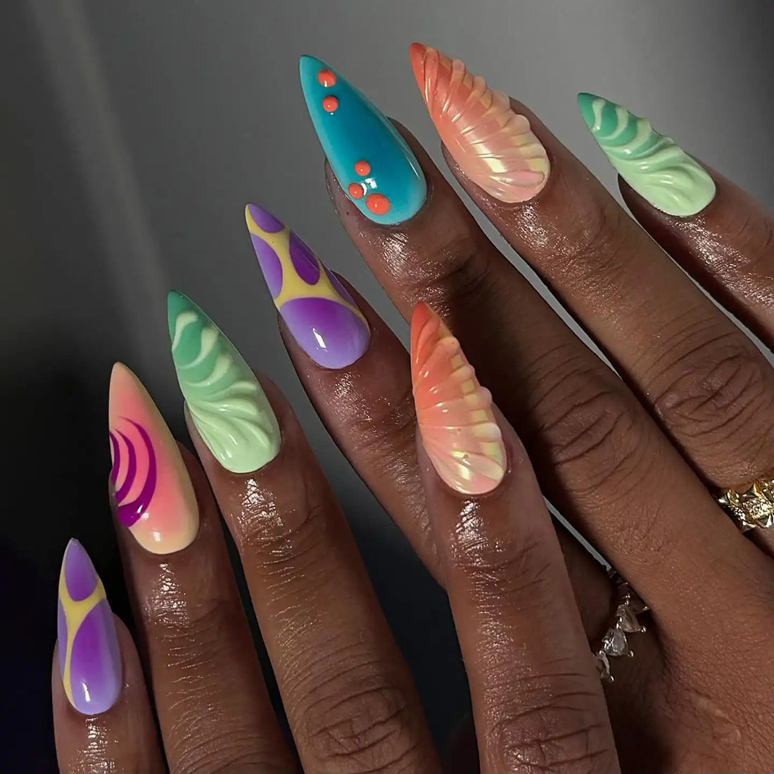 Hand with handmade colorful press-on nails featuring swirls, shell patterns, and summer designs.