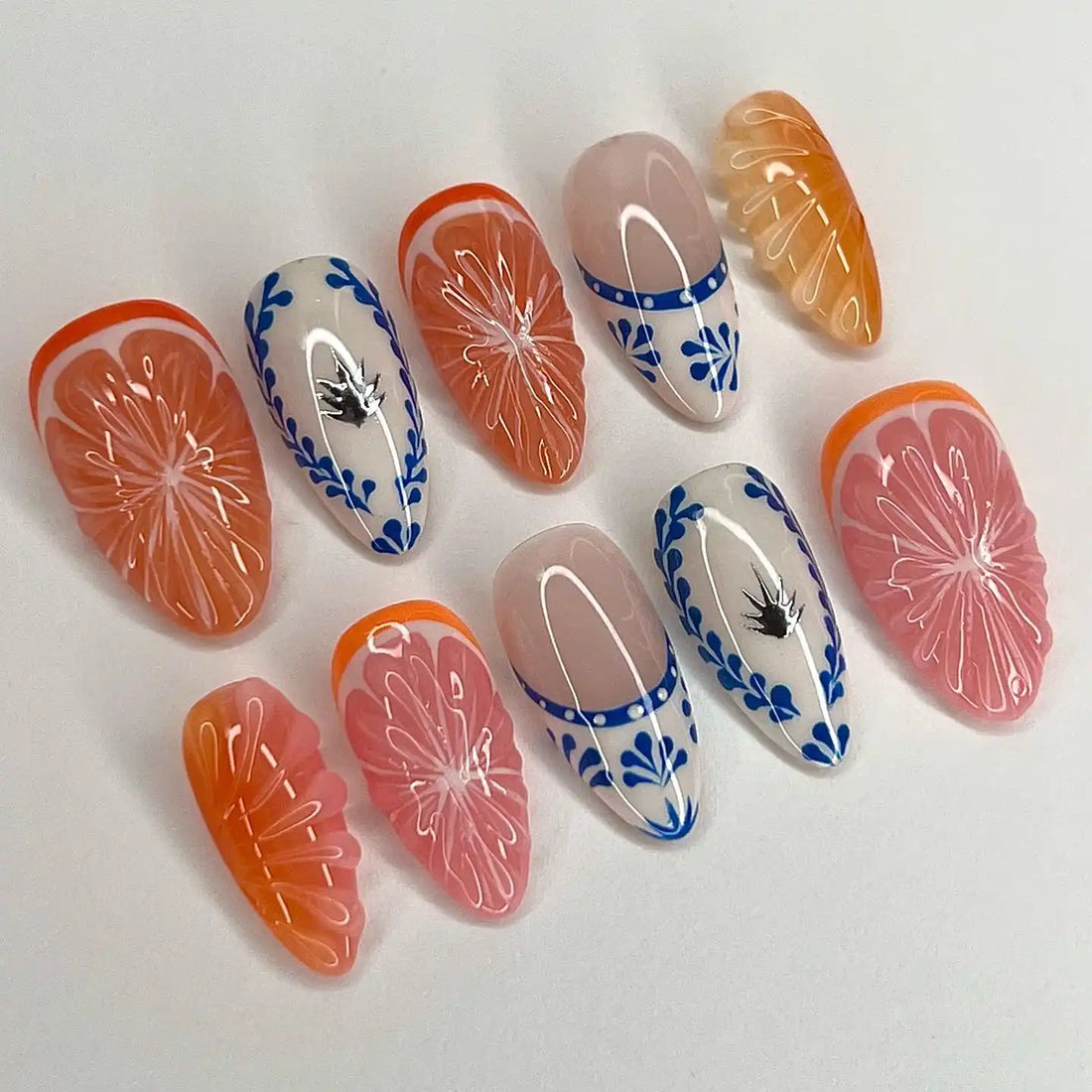 Handmade press-on nails with orange and pink fruit designs, blue floral accents, and glossy finish.