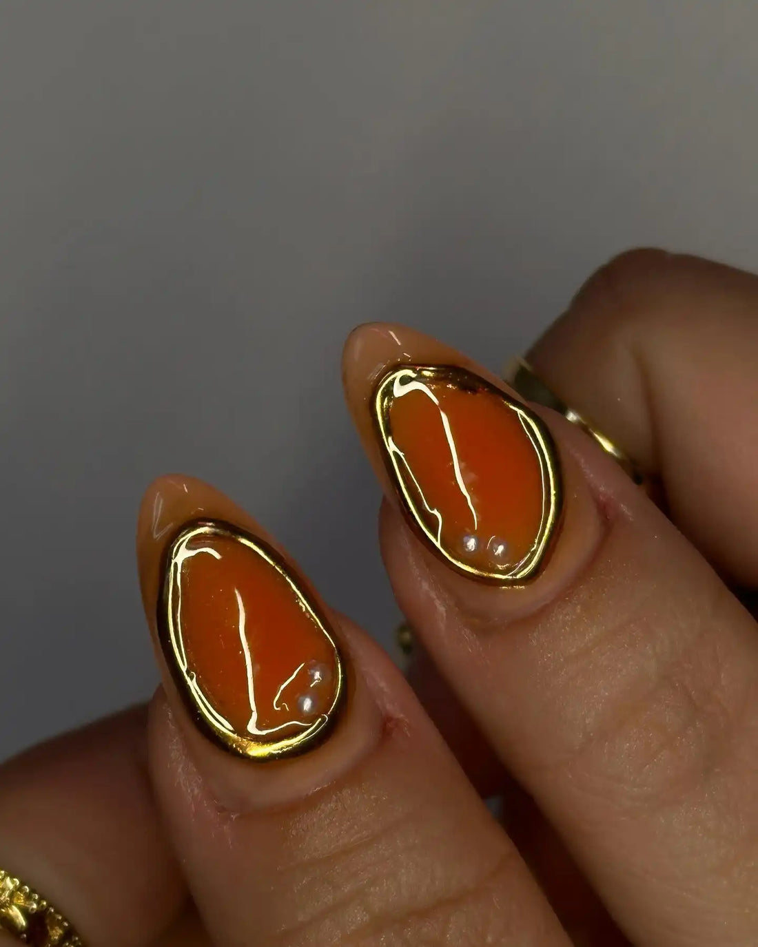 Handmade press-on nails with orange shell design and gold accents on manicured hands