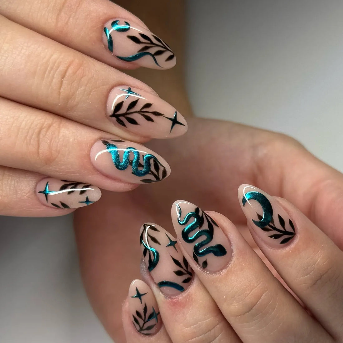 Handmade press-on nails with teal chrome snake, moon, black leaves, and celestial designs
