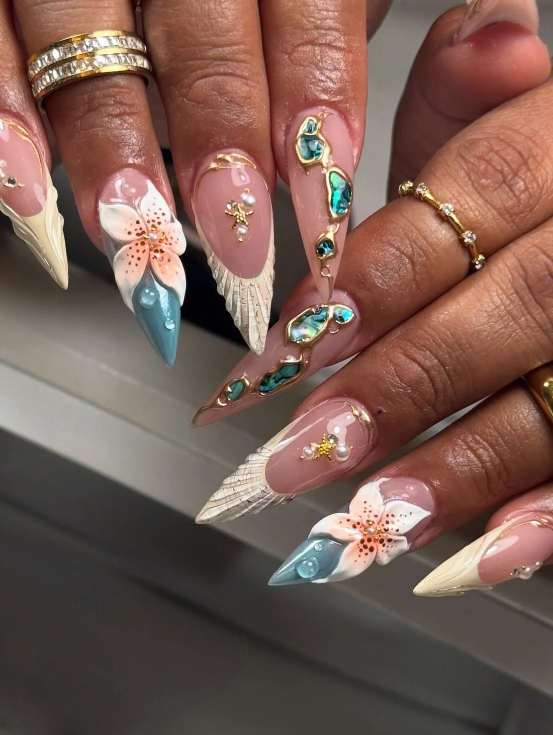Hand with long handmade press-on nails featuring teal, abalone, flower, and shell designs.