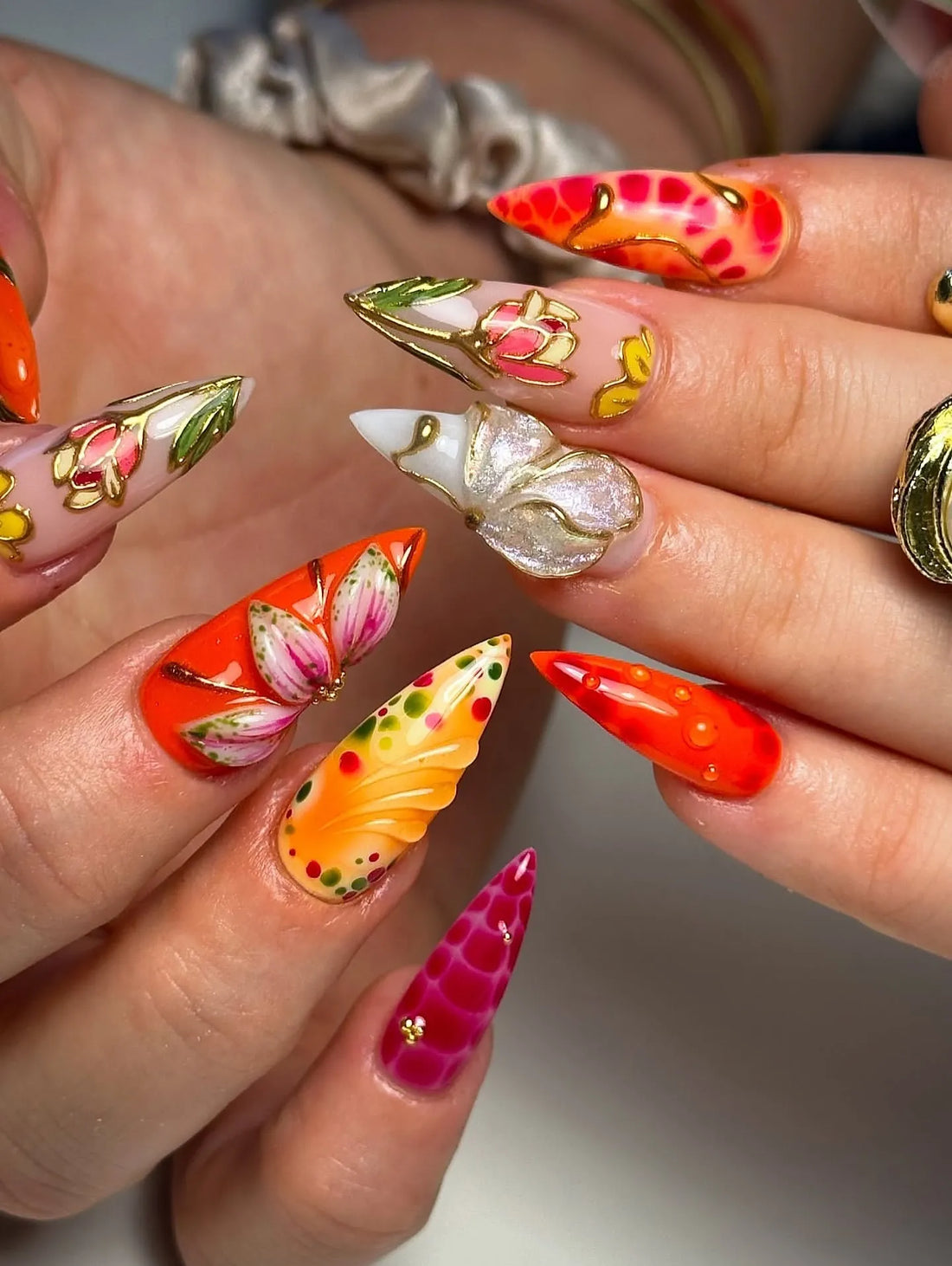 Handmade tropical press-on nails with orange, pink, floral designs and gold foil accents