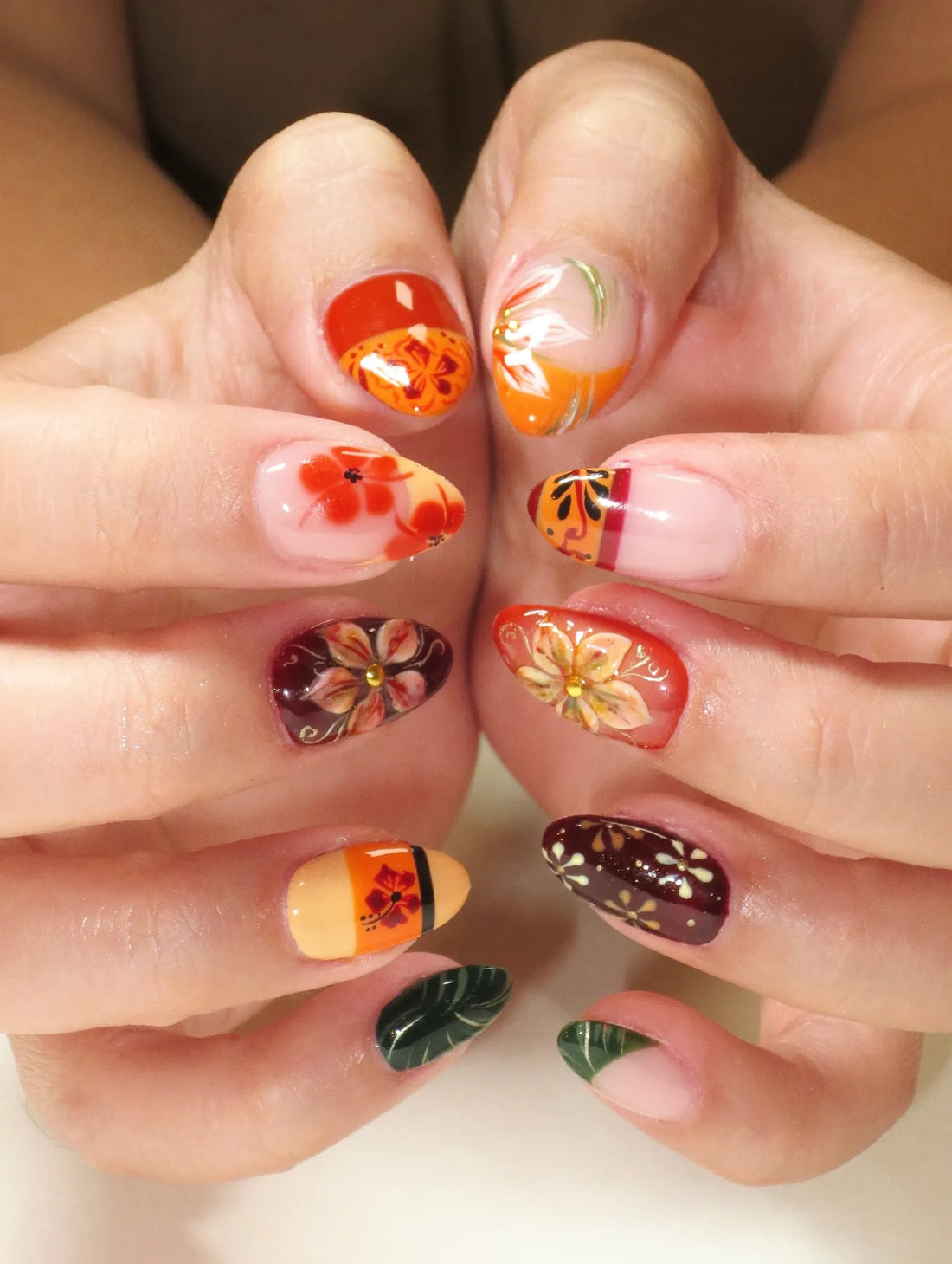 Hand with handmade press-on nails featuring tropical hibiscus and autumn floral designs in multicolor.