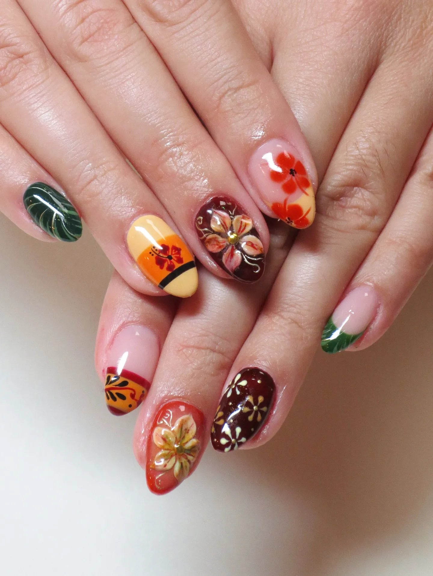 Hand with handmade press-on nails featuring tropical hibiscus and autumn floral designs in multicolor.