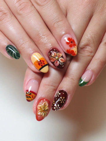 Hand with handmade press-on nails featuring tropical hibiscus and autumn floral designs in multicolor.