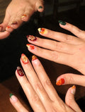 Hand with multicolor handmade press-on nails featuring tropical hibiscus and autumn floral designs.