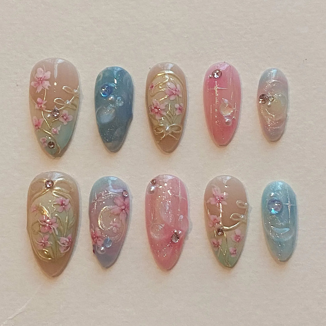 Handmade press-on nails with pastel pink and blue floral designs and rhinestone accents