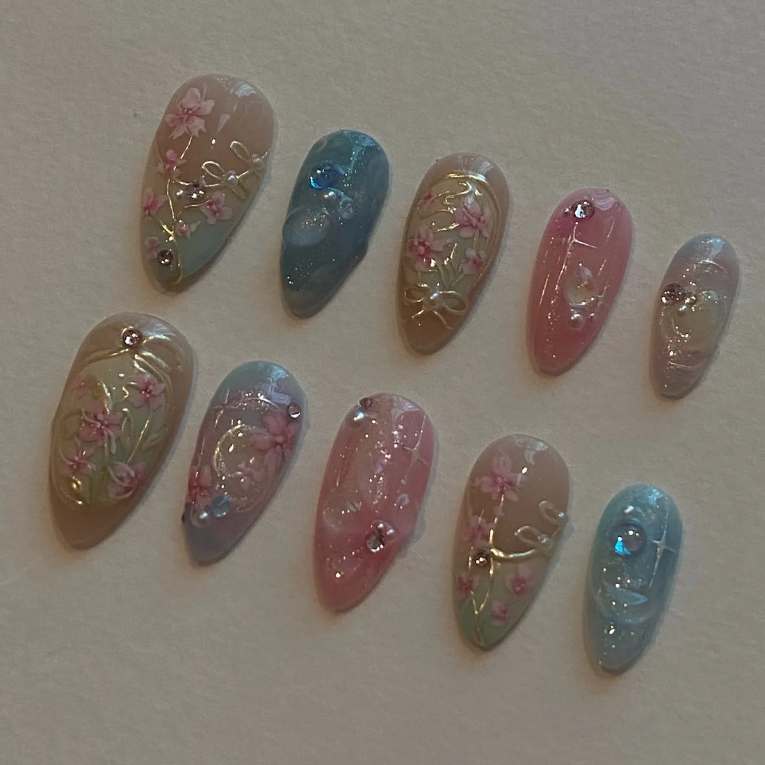 Handmade press-on nails with pastel pink and blue floral designs and rhinestone accents