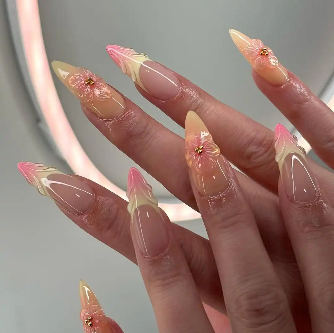 Hand with long almond-shaped press-on nails in pink and yellow with 3D floral design.