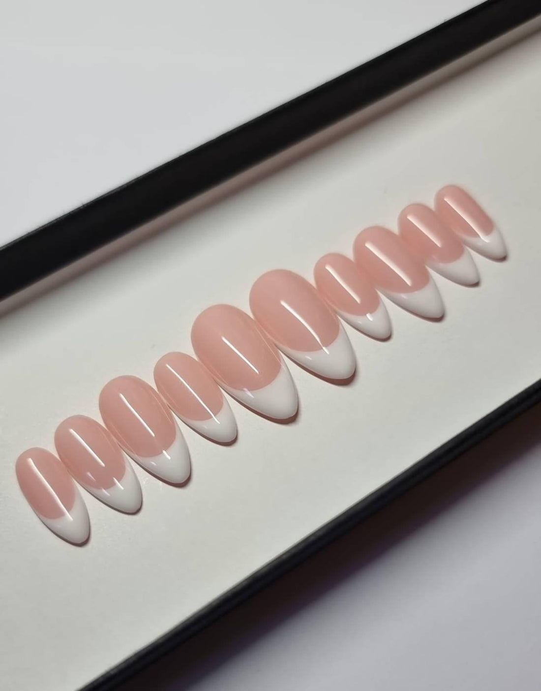 Hand displaying handmade white French tip press-on nails with almond shape