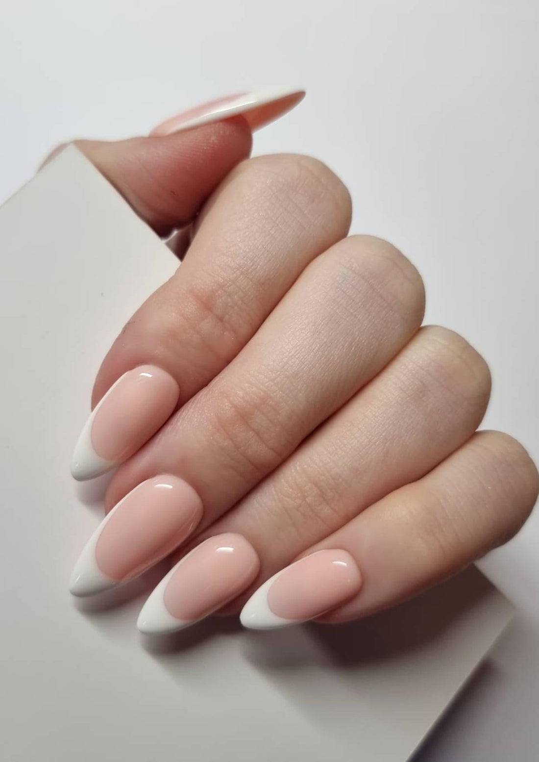 Hand displaying handmade white French tip press-on nails with almond shape