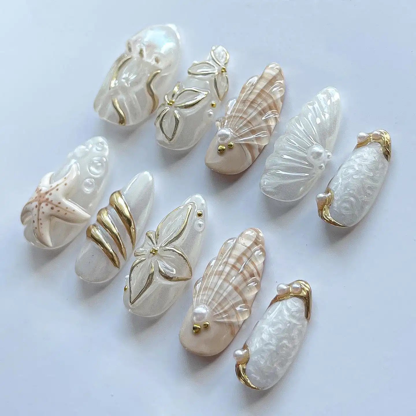 Handmade white and gold ocean-themed press-on nails with seashell, starfish, and jellyfish designs.
