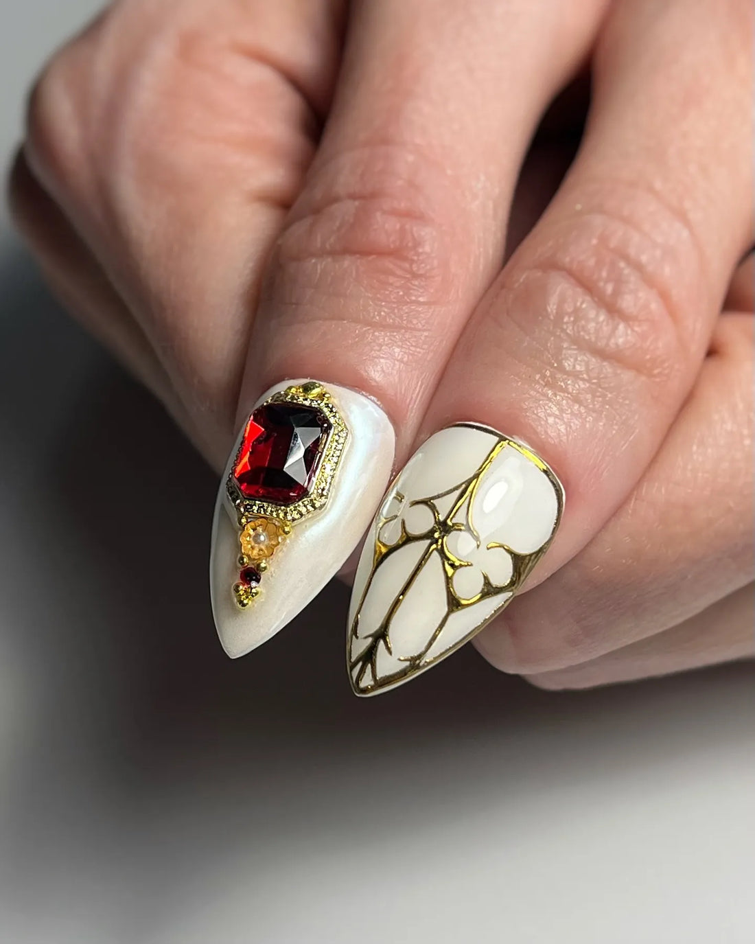 Handmade white stiletto press-on nails with gold gothic cross, pearl, and red gem accents