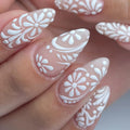 Hand with almond-shaped press-on nails featuring white lace floral swirl designs, elegant bridal style.