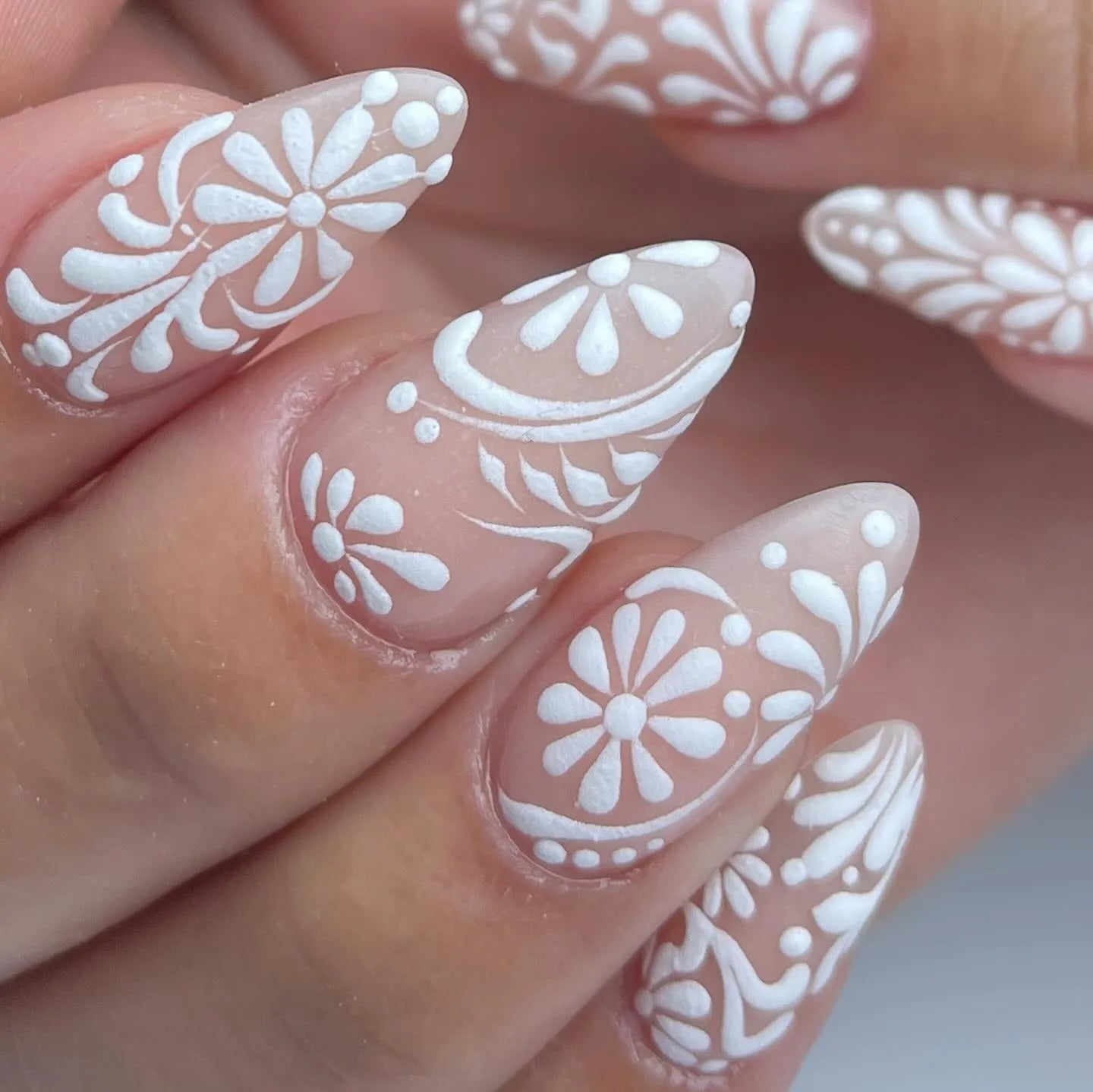Hand with almond-shaped press-on nails featuring white lace floral swirl designs, elegant bridal style.