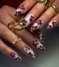 Hand with long white and pink floral press-on nails with gold accents and artistic dots