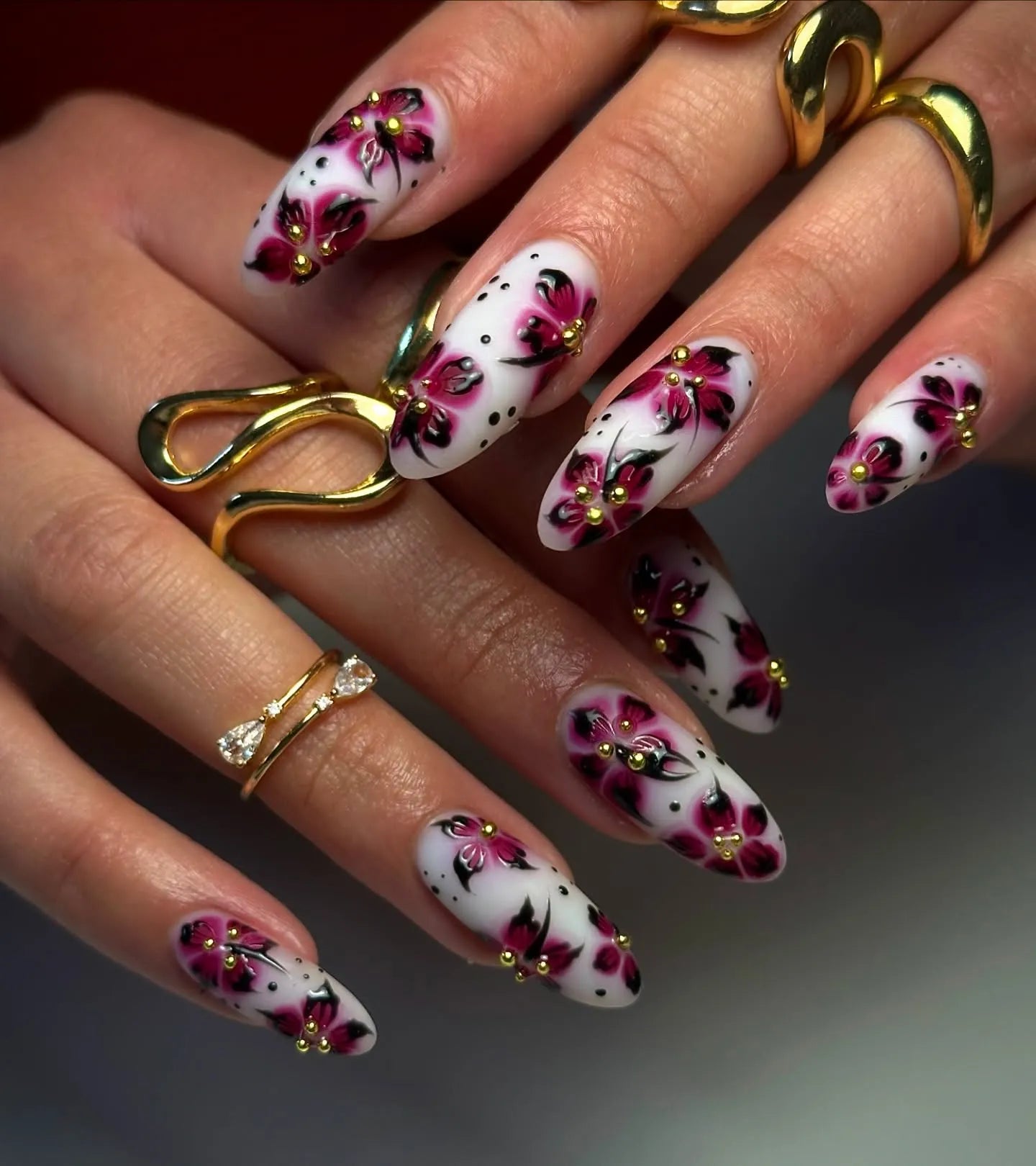 Hand with long white and pink floral press-on nails with gold accents and artistic dots