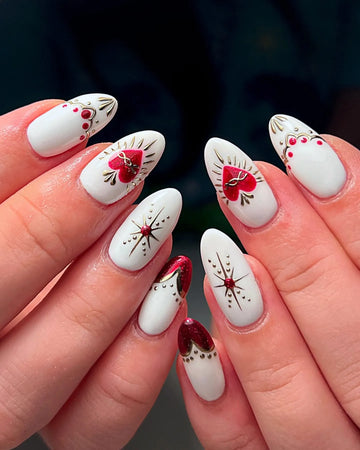 White press-on nails with red heart accents, gold filigree, and gemstone details.