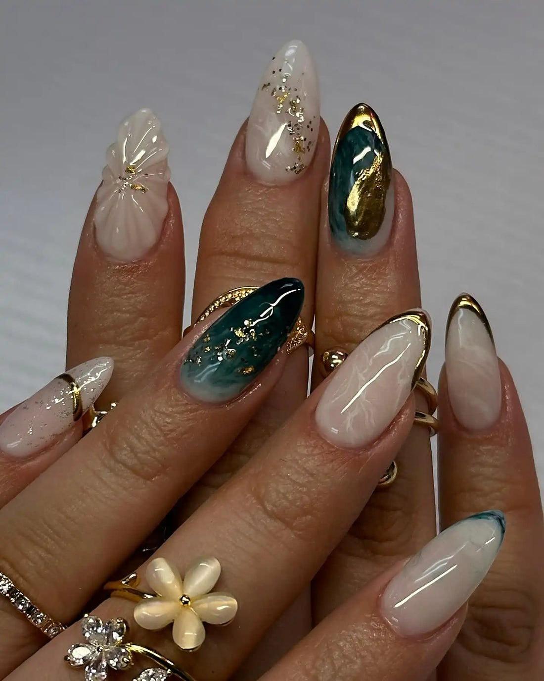 Handmade white and emerald green press-on nails with gold foil accents, floral detail, and glossy finish.