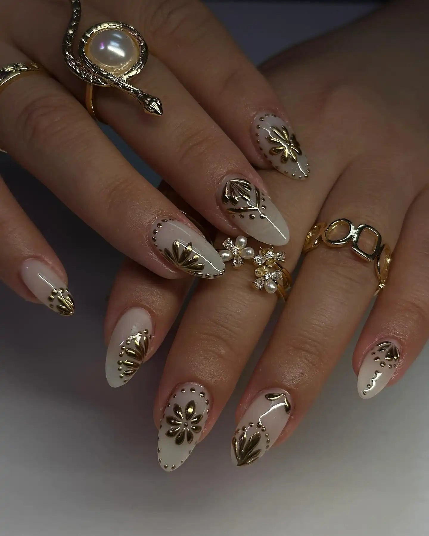 Hand with glossy white press-on nails featuring 3D gold floral accents and elegant details.