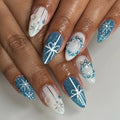 Blue and white winter holiday press-on nails with snowflakes, bows, and glitter accents