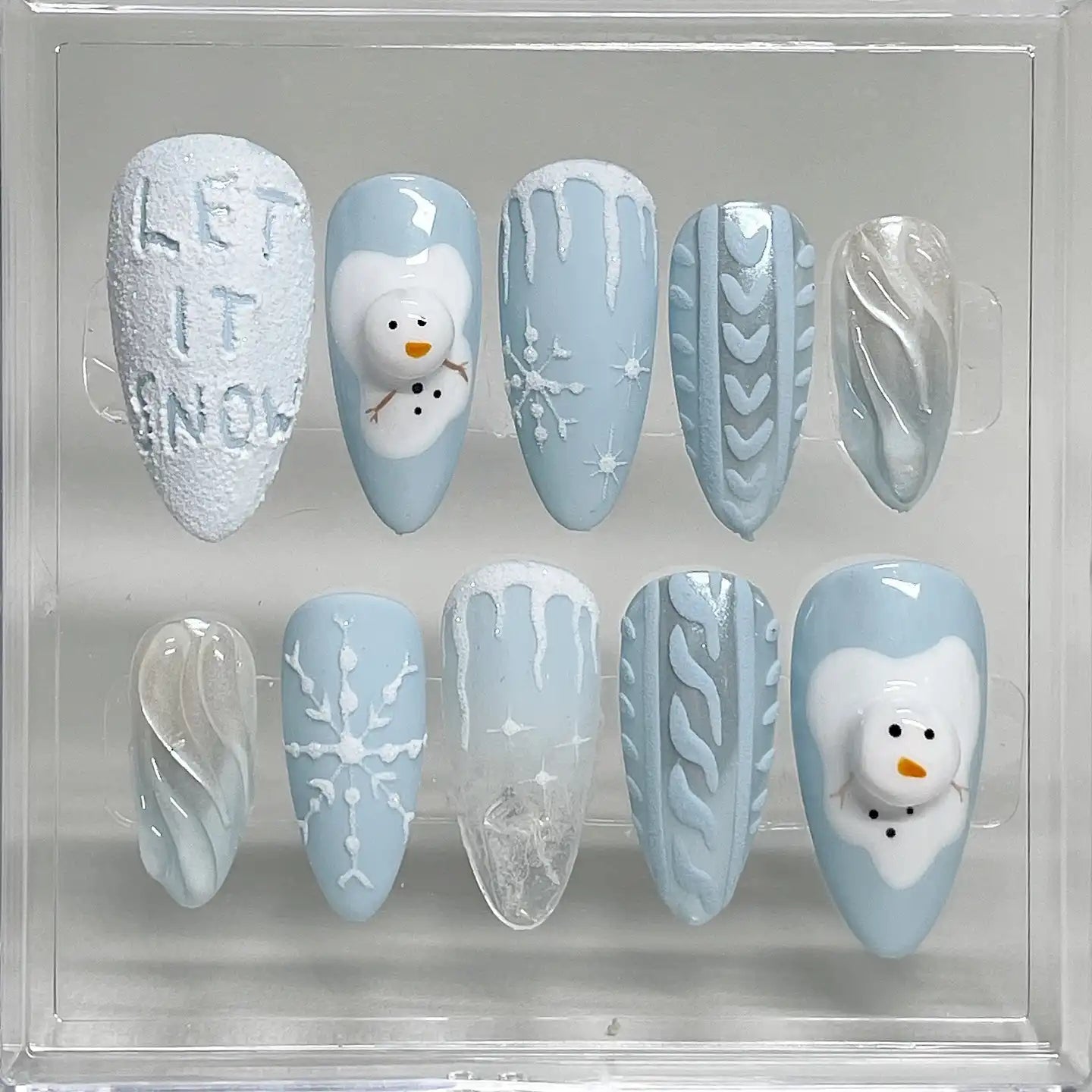 Handmade blue winter press-on nails with snowman, snowflake, icicle and sweater designs.