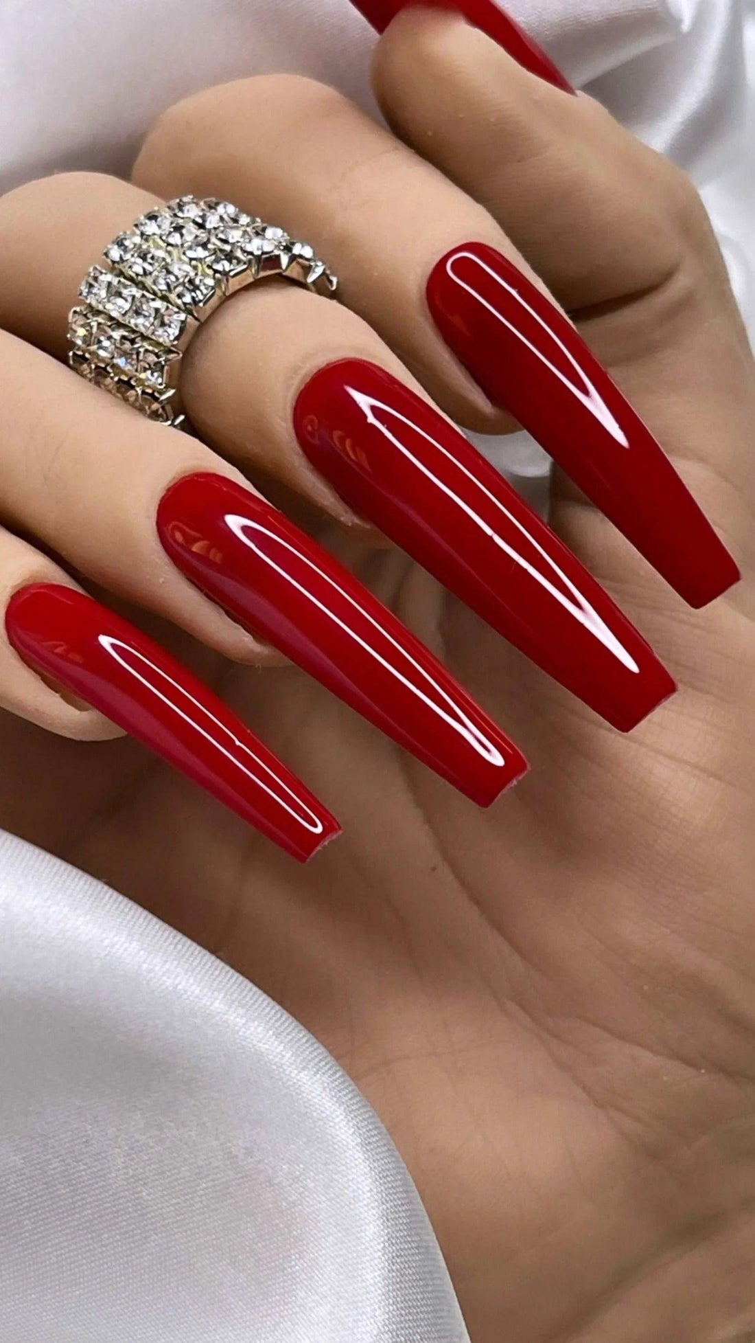 Hand with long coffin-shaped glossy red press-on nails and a rhinestone ring