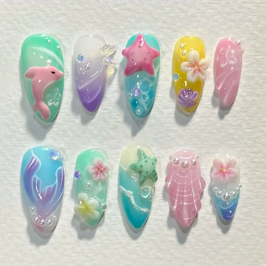Ocean themed press-on nails with 3D dolphin, starfish, seashell, mermaid tail, and floral designs.
